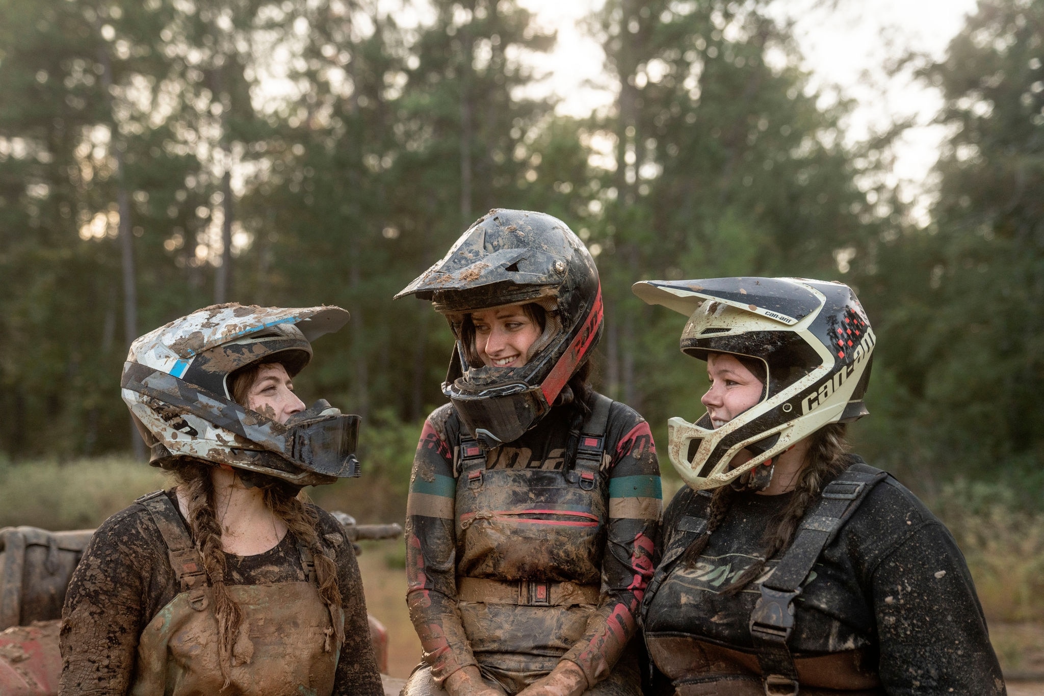 Three women wearing Can-Am branded riding gear covered in mud