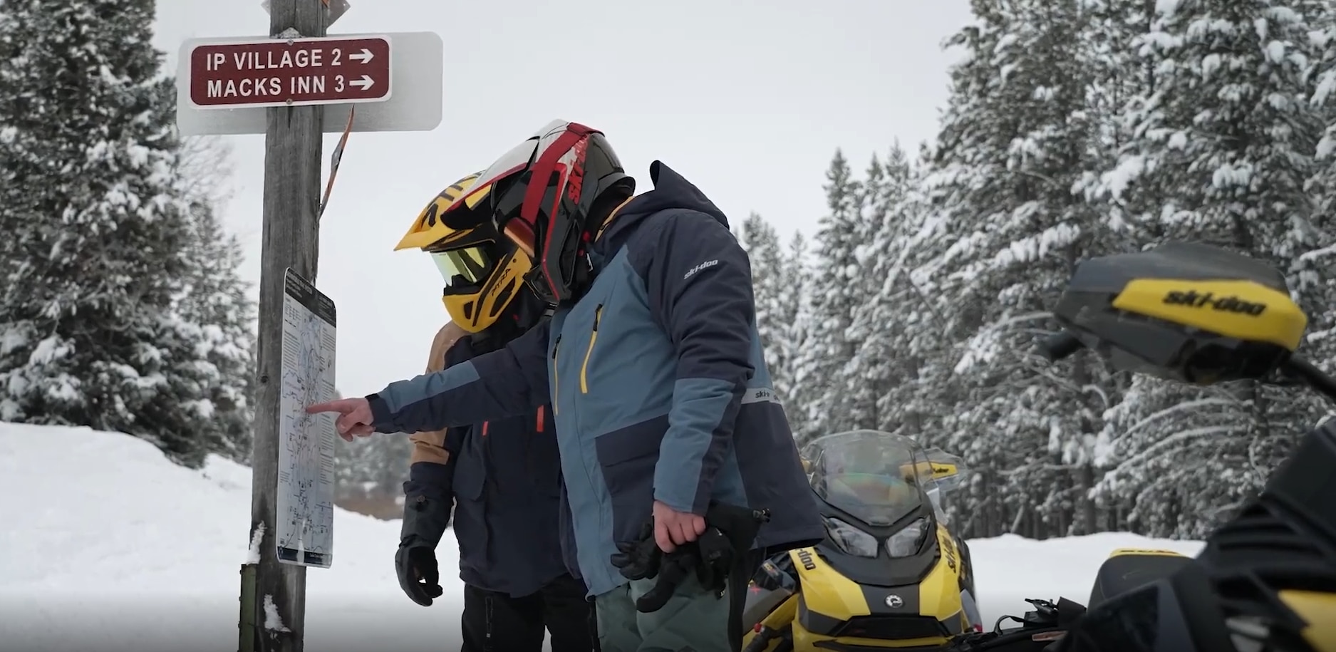Deux motoneigistes Ski-Doo qui regardent leur itinéraire sur un sentier enneigé