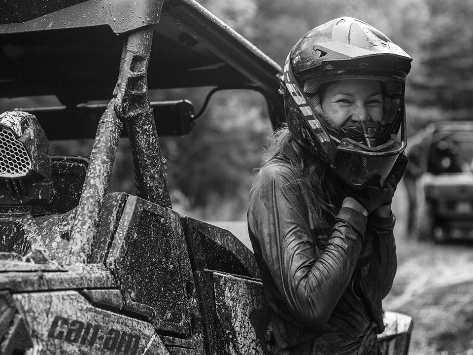 Woman untying her protective helmet next to a muddy Can-Am SxS
