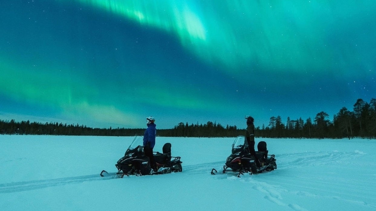Deux motoneigistes observant une aurore boréale