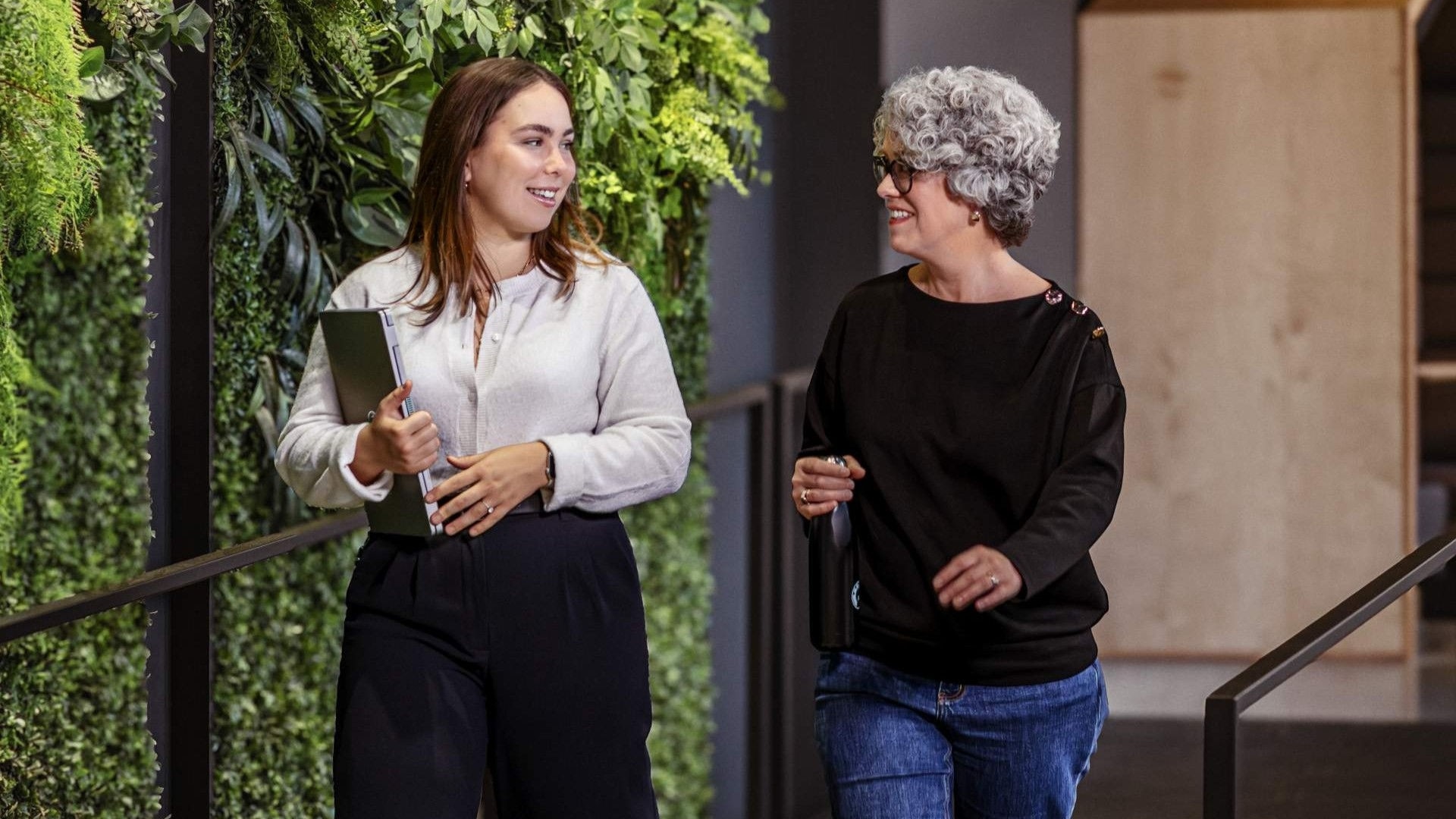 Two BRP professionals in a business discussion by a green wall in a modern office.