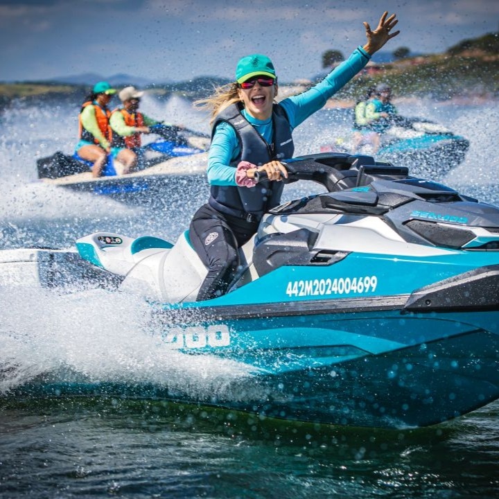 Five people on three BRP Sea-Doo personal watercraft, with the lead rider waving during a group ride.