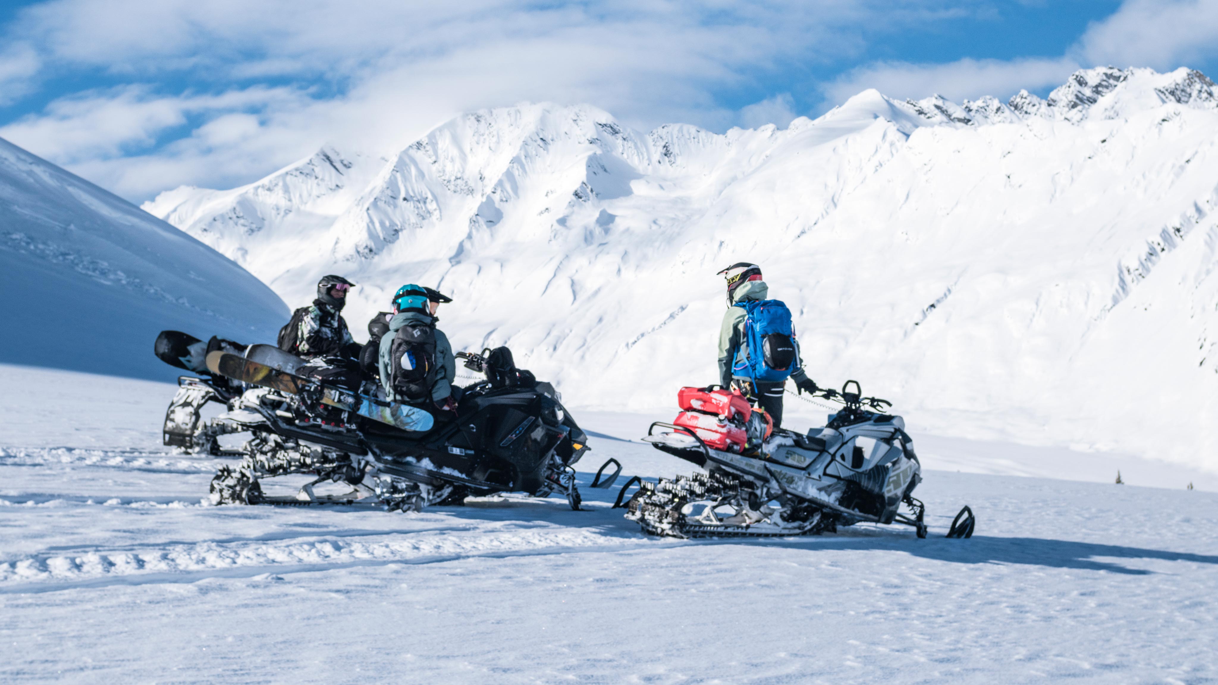 Three snowmobilers take a break on a snowy mountain