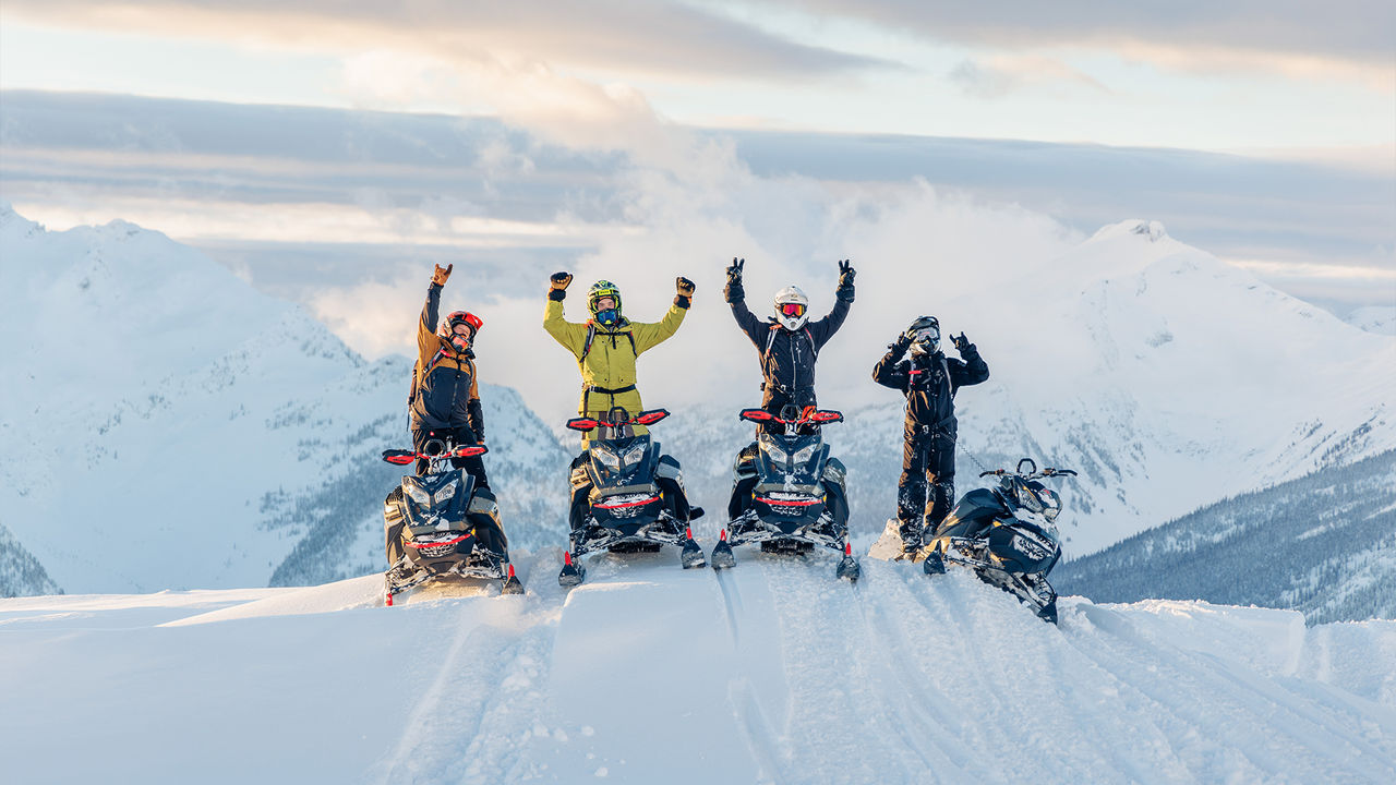 Cuatro pilotos de motos de nieve en la cima de una montaña nevada