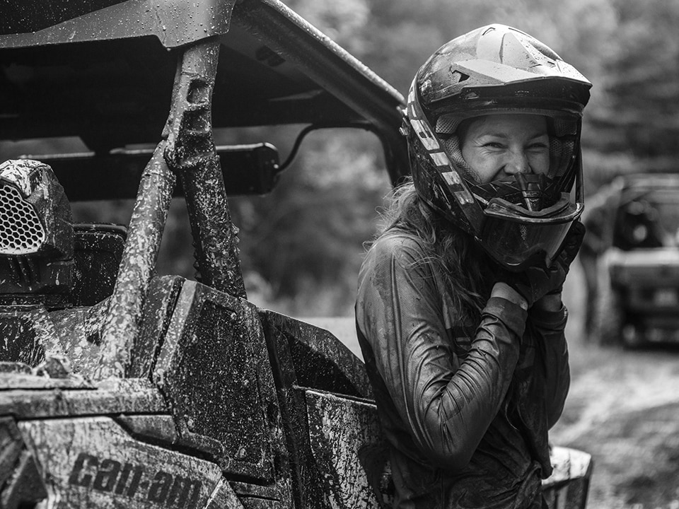 Mujer desatándose el casco protector junto a una Can-Am SxS embarrada