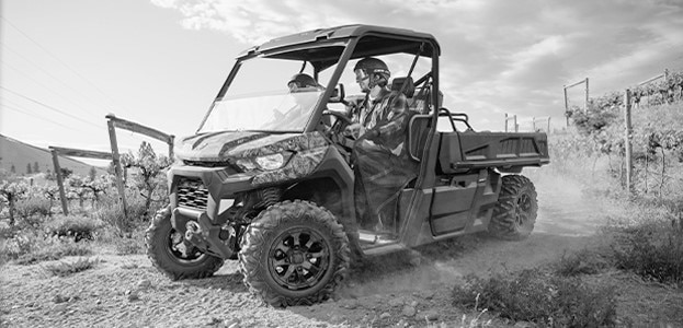 Two people riding a Can-Am Defender side-by-side vehicle